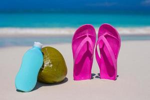 Flip Flops, Kokosnuss und Sonnencreme auf weißem Sand foto