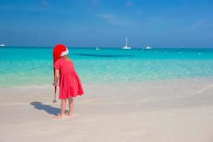 kleines süßes Mädchen in roter Weihnachtsmütze am Strand foto