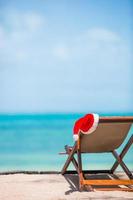 Sonnenliegen mit Weihnachtsmütze am wunderschönen tropischen Strand mit weißem Sand und türkisfarbenem Wasser. perfekter weihnachtsurlaub foto