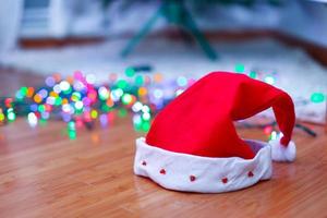 Nahaufnahme der roten Weihnachtsmütze auf dem Boden im mehrfarbigen Girlandenhintergrund foto