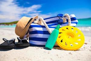 Streifentasche, Strohhut, Sonnencreme und Handtuch am Strand foto
