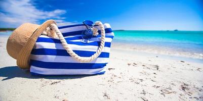 Streifentasche, Strohhut, Sonnencreme und Handtuch am weißen tropischen Strand foto