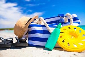 Streifentasche, Strohhut, Sonnencreme und Handtuch am Strand foto