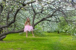 kleines entzückendes mädchen, das auf blühendem apfelbaum sitzt foto