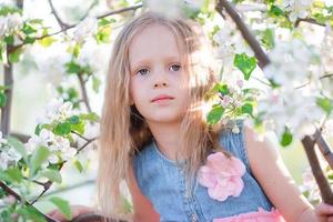 Porträt eines kleinen Mädchens im blühenden Apfelbaumgarten am Frühlingstag foto