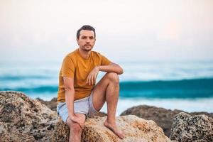 junger Mann, der sich bei Sonnenuntergang am Strand entspannt foto