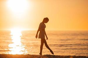 Silhouette des schönen Mädchens, das einen wunderschönen Sonnenuntergang am Strand genießt foto