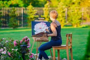 glückliche Frau, die an einem warmen Tag ein Bild auf einer Staffelei malt foto