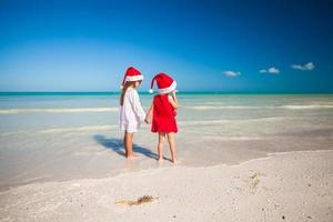 Rückansicht von kleinen süßen Mädchen in Weihnachtsmützen am exotischen Strand foto
