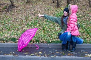 Kleines Mädchen und ihre Mutter gehen an einem regnerischen Tag mit Regenschirm spazieren foto