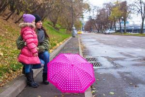 Kleines Mädchen und ihre Mutter gehen an einem regnerischen Tag mit Regenschirm spazieren foto