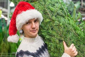 mann in weihnachtsmütze kauft weihnachtsbaum und zeigt daumen hoch foto
