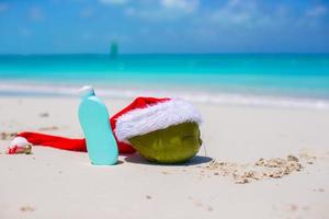 sonnencreme und weihnachtsmütze auf kokosnuss am weißen exotischen strand foto