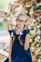 entzückendes kleines Schulmädchen mit grünem Apfel im Freien. zurück zum schulkonzept foto