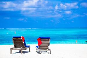 roter weihnachtsstrumpf und weihnachtsmütze auf stuhl am tropischen weißen strand foto