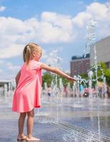 Kleines Mädchen, das an heißen sonnigen Tagen im offenen Straßenbrunnen spielt foto
