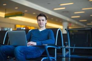 junger Mann mit einem Laptop am Flughafen, während er seinen Flug wartet foto