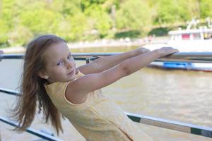 Kleines entzückendes Mädchen auf dem Deck eines Schiffes, das in der Großstadt segelt foto
