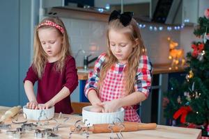 Kleine Mädchen machen Weihnachtslebkuchenhaus am Kamin im dekorierten Wohnzimmer. foto