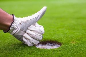 Die Hand der Männer in einem Handschuhgolf zeigt in der Nähe des Lochs ok foto