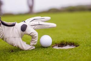 Nahaufnahme der Hand eines Mannes, der Golfball in Loch auf Kurs setzt foto