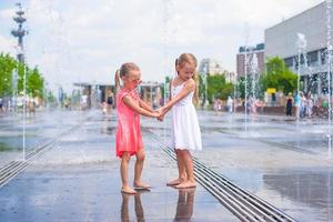 Kleine Mädchen genießen den sonnigen Tag im Brunnen im Freien foto