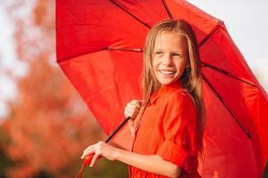 glückliches Kindermädchen lacht unter rotem Regenschirm foto