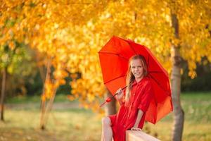 glückliches Kindermädchen lacht unter rotem Regenschirm foto