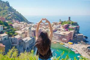 schönes mädchen, das mit händen herzform auf dem alten küstenstadthintergrund von vernazza, nationalpark cinque terre, ligurien, italien, europa macht foto