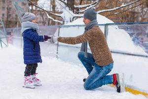 entzückendes kleines Mädchen und glücklicher Vater auf der Eisbahn im Freien foto