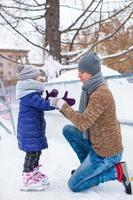 entzückendes kleines Mädchen und glücklicher Vater auf der Eisbahn im Freien foto