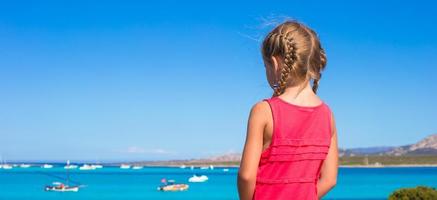 Kleines entzückendes Mädchen, das einen wunderschönen Blick auf das türkisfarbene Meer genießt foto