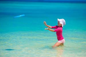 kleines Mädchen spielt mit Flugscheibe am weißen Strand foto