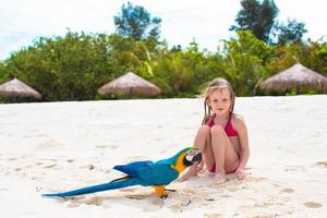 entzückendes kleines Mädchen am Strand mit großem buntem Papagei foto