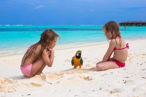 Entzückende kleine Mädchen am Strand mit großem buntem Papagei foto