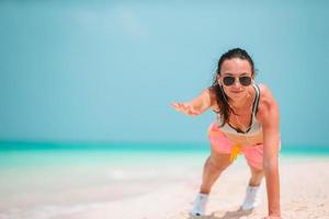 Fitte junge Frau, die in ihrer Sportkleidung Übungen am tropischen weißen Strand macht foto