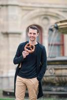 schöner junger Mann, der Brezel hält und sich im Park entspannt foto