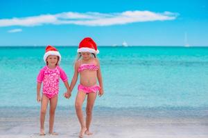 kleine entzückende mädchen in weihnachtsmützen während des strandurlaubs haben spaß zusammen foto