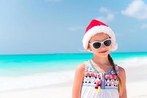 entzückendes kleines mädchen in weihnachtsmütze während der weihnachtsferien am strand foto