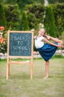 glückliches kleines Schulmädchen mit einer Tafel im Freien foto