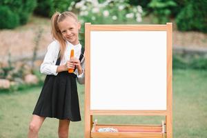 glückliches kleines Schulmädchen mit einer Tafel im Freien foto