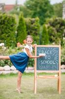 glückliches kleines Schulmädchen mit einer Tafel im Freien foto