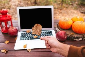 orange Kürbis und Blätter in der Nähe von Laptop-Computer auf einem Tisch. Zeit der Herbstsaison foto