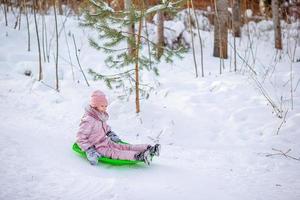 Entzückendes kleines glückliches Mädchen, das im verschneiten Wintertag Rodeln fährt. foto
