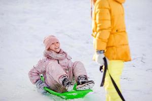 Entzückende kleine glückliche Mädchen, die im verschneiten Wintertag Rodeln. foto