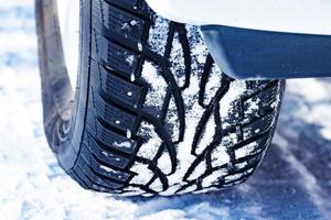 Nahaufnahme eines mit Schnee bedeckten Spikereifens auf einer verschneiten Straße im Winter foto