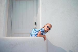 charmantes mädchen im freien in alten straßen und mykonos. Kind auf der Straße eines typischen griechischen traditionellen Dorfes mit weißen Wänden und bunten Türen auf der Insel Mykonos in Griechenland foto