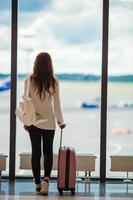 junge Frau in der Nähe des Fensters in einer Flughafenlounge, die auf die Ankunft wartet foto