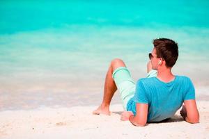 glücklicher junger Mann, der die Musik am weißen Sandstrand genießt foto