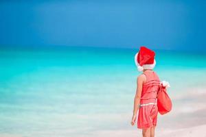 entzückendes kleines Mädchen in der Weihnachtsmütze am tropischen Strand foto